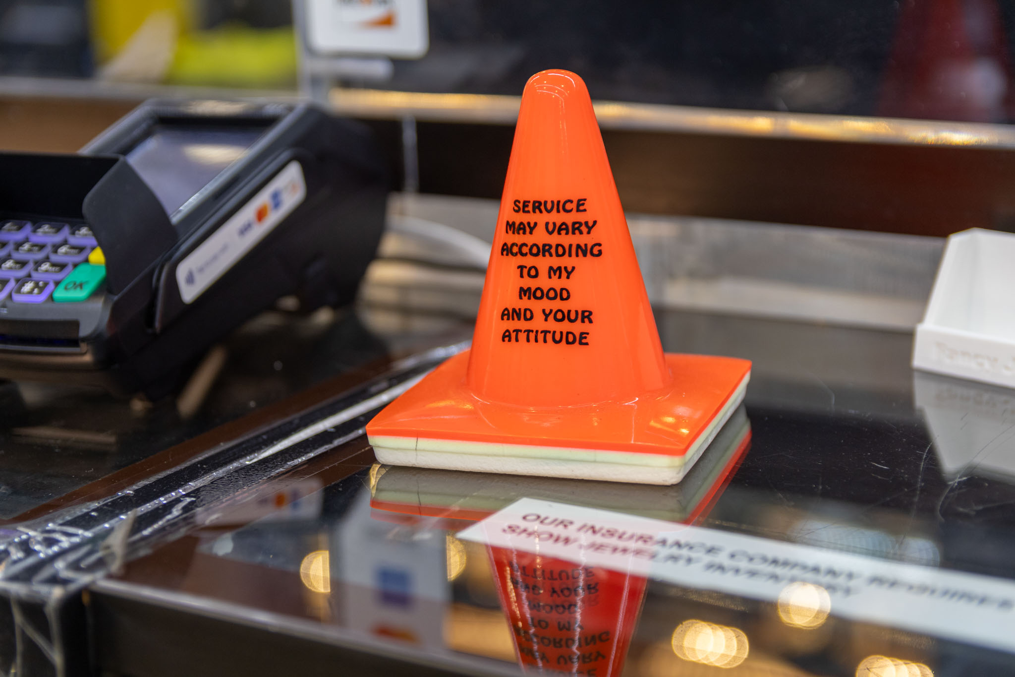 A small comedic traffic cone sitting on a desk that reads " Service may vary according to my mood and your attitude"